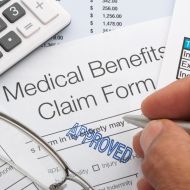 Person writing on a medical benefits claim form that has been stamped Approved